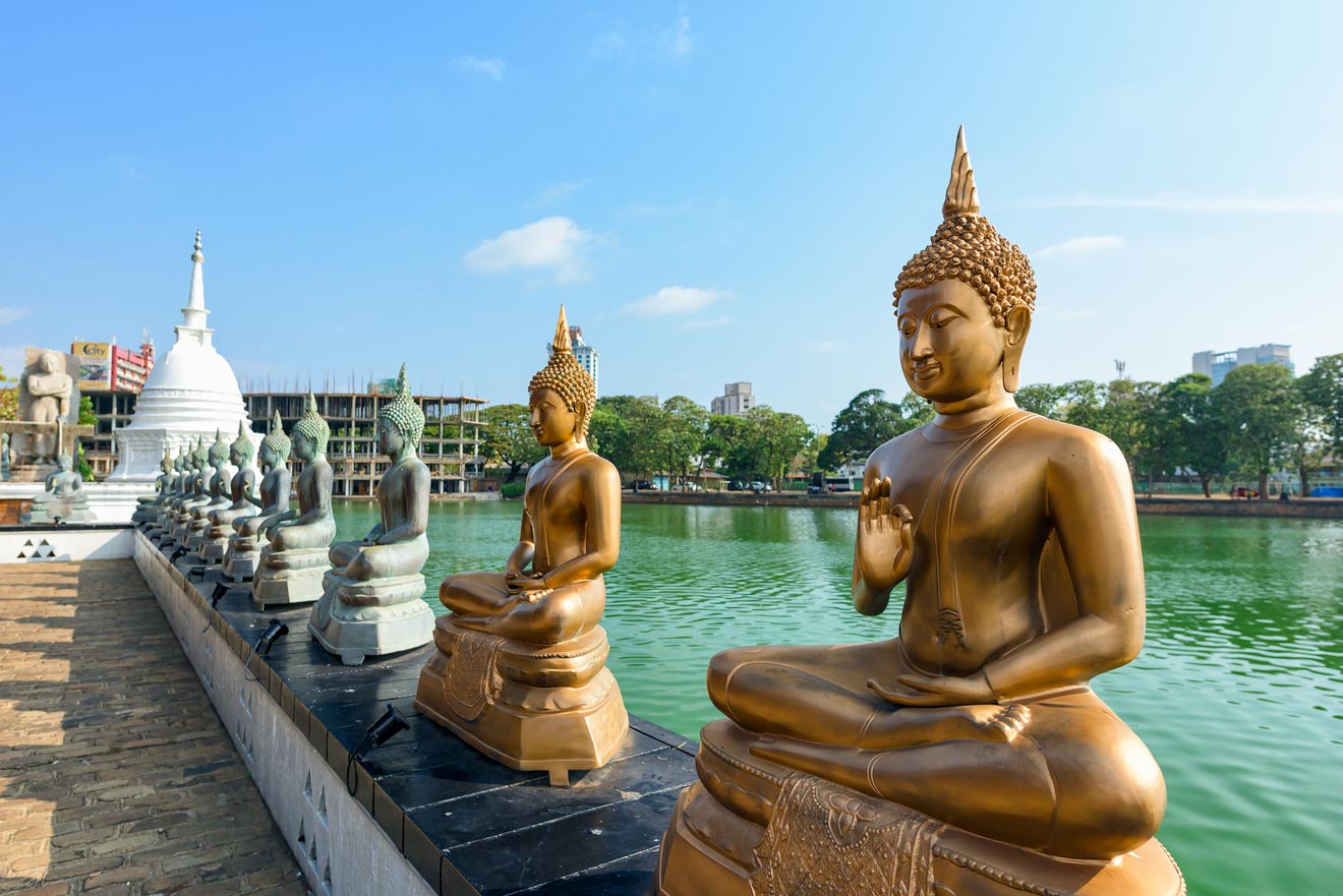 A serene row of golden Buddha statues in meditation pose, overlooking a tranquil lake with a white stupa in the background, under a bright blue sky, evoking a sense of peace and spirituality.