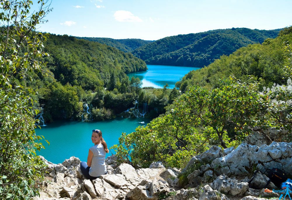 The writer of the post sitting on rocky outcrop enjoying a breathtaking view of the turquoise lakes and cascading waterfalls at Plitvice Lakes National Park