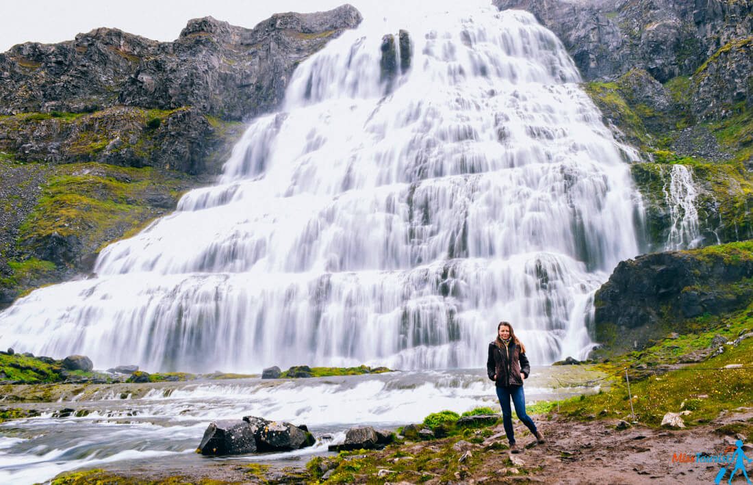 The author of the post is standing on a rocky area in front of a large multi-tiered waterfall falling from the side of a mountain.