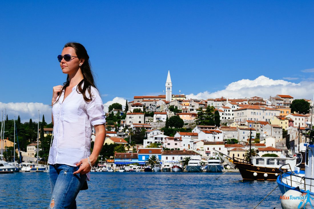 The writer of the post standing at the waterfront, with the picturesque hilltop town of Vrsar, Croatia, and its marina in the background