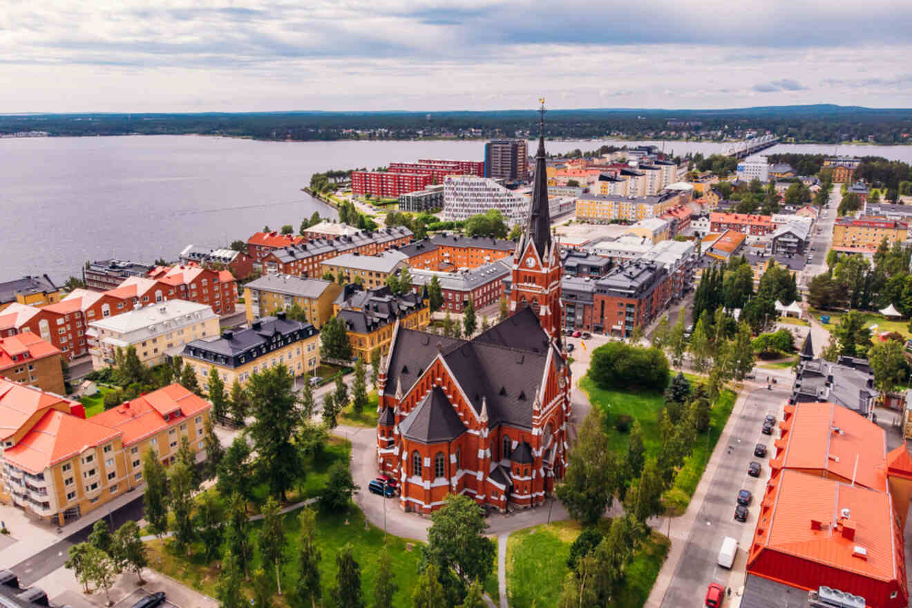 Aerial view of a cityscape with a prominent church featuring a tall spire in the foreground, surrounded by colorful buildings and a lake in the background.