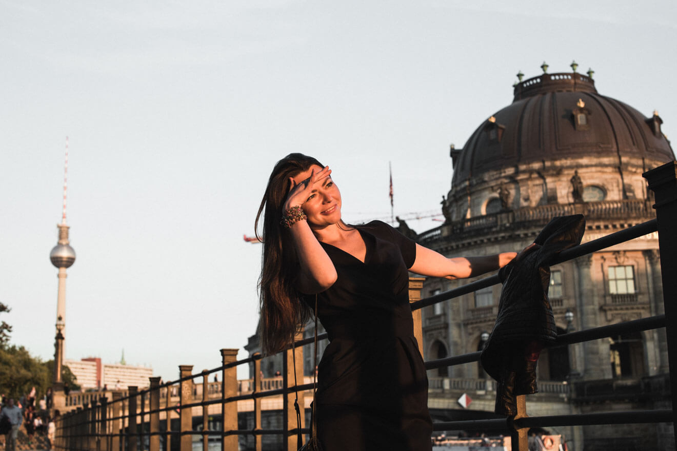 Yulia, the author, in a black dress leaning against a railing in Mitte.