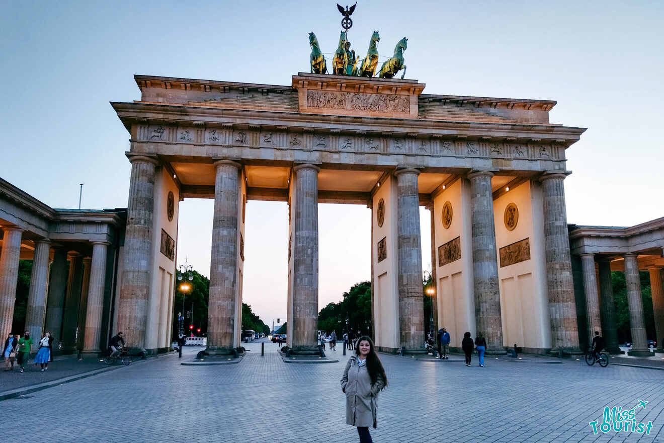 A person stands in front of the Brandenburg Gate in Berlin during evening light.