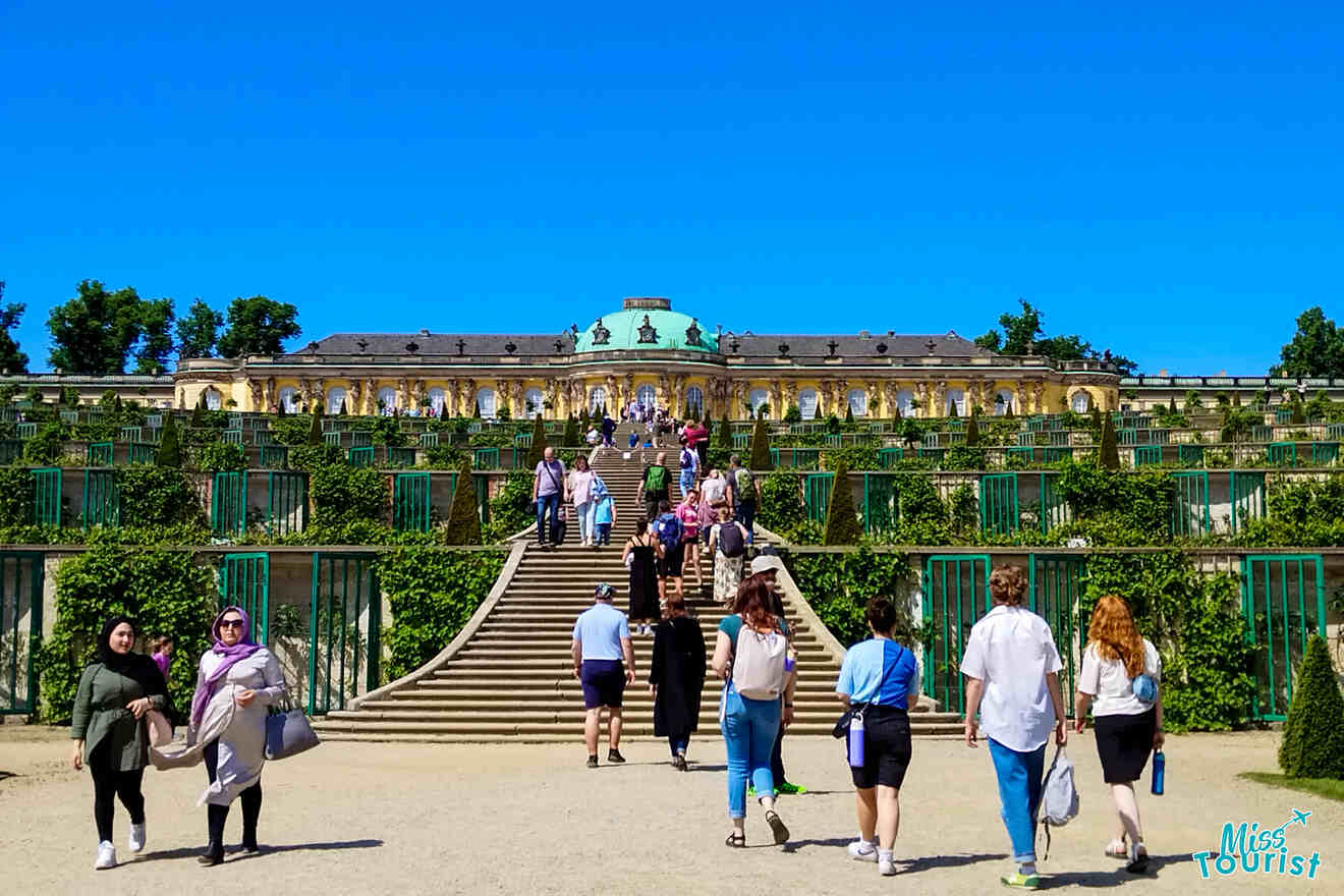 Tourists visit the terraced gardens leading to Sanssouci Palace in Potsdam, Germany, under a clear blue sky.