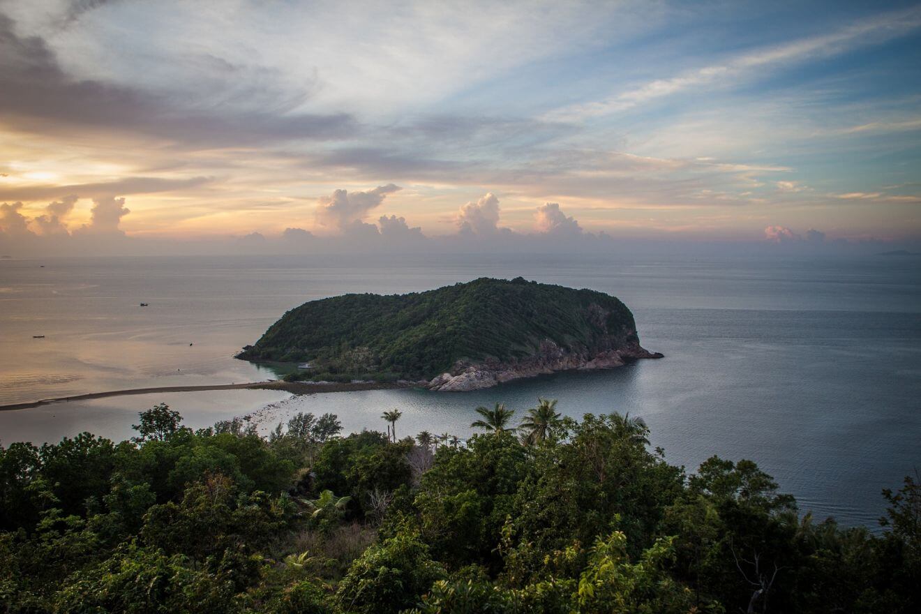 Elevated view of the lush green island of Koh Phangan surrounded by the calm sea at dusk, with clouds softly lit by the fading sunlight