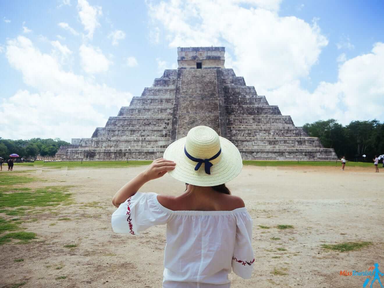 a woman in a white hat standing in front of a pyramid Chichen Itza