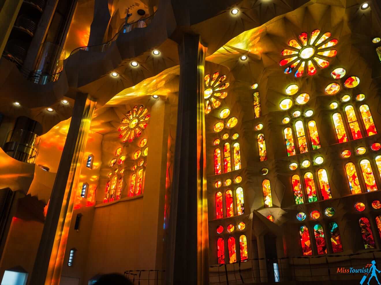 Interior view of a cathedral with tall columns, colorful stained glass windows, and illuminated light patterns on the walls.