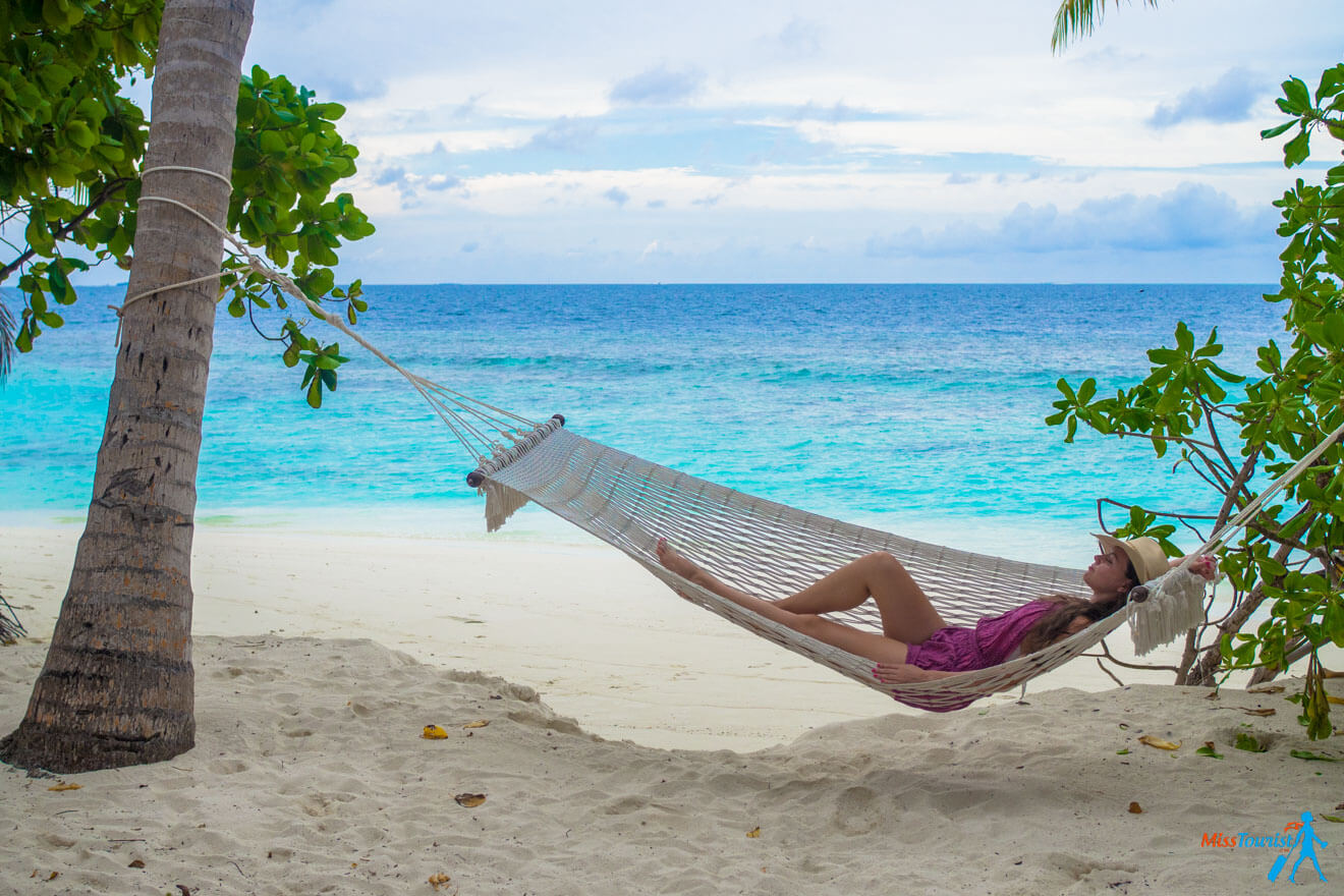 The writer of the post relaxing in a hammock tied between two palm trees on a sandy beach with turquoise ocean water in the background.