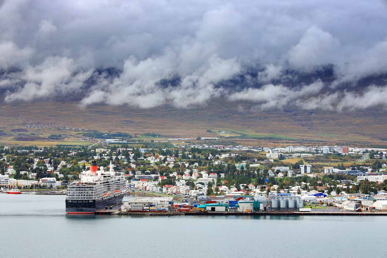 Panoramic view of Akureyri, Iceland's picturesque town with colorful buildings, set against a backdrop of mountains and low-hanging clouds, with a large cruise ship docked at the harbor