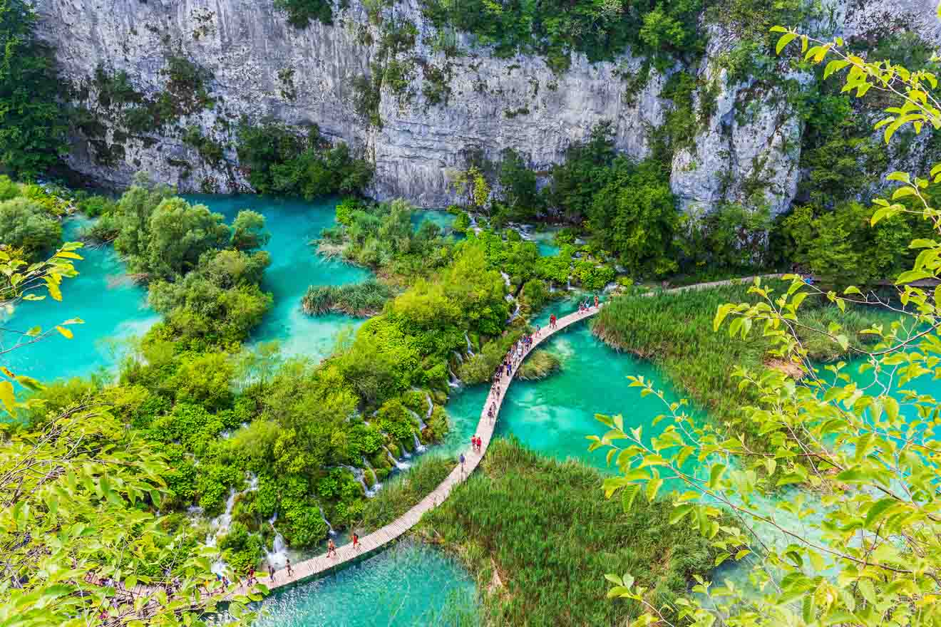 Elevated view of a winding boardwalk over the bright turquoise waters of Plitvice Lakes with dense green foliage
