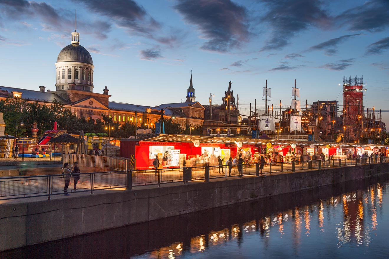 Evening view of a vibrant outdoor market near a historic dome-topped building and amusement park in Montreal, reflecting city life at dusk.