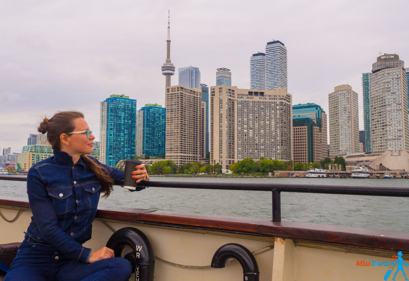 The author of the post in a denim jacket and glasses holds a drink while sitting on a boat, with a city skyline featuring tall buildings and a prominent tower in the background.