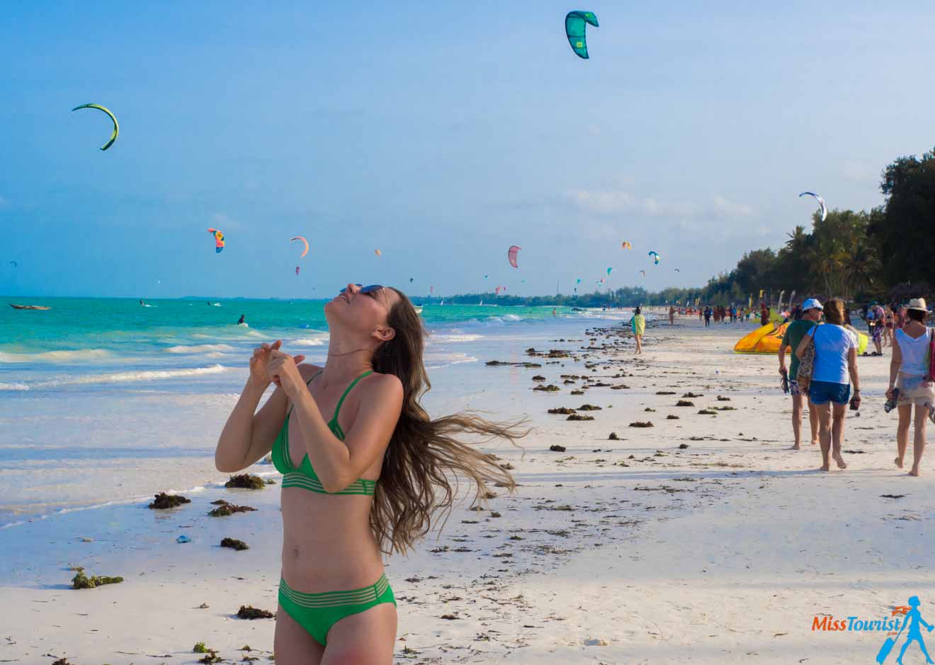 A woman in a green bikini on Paje beach in Zanzibar with paragliders in the background