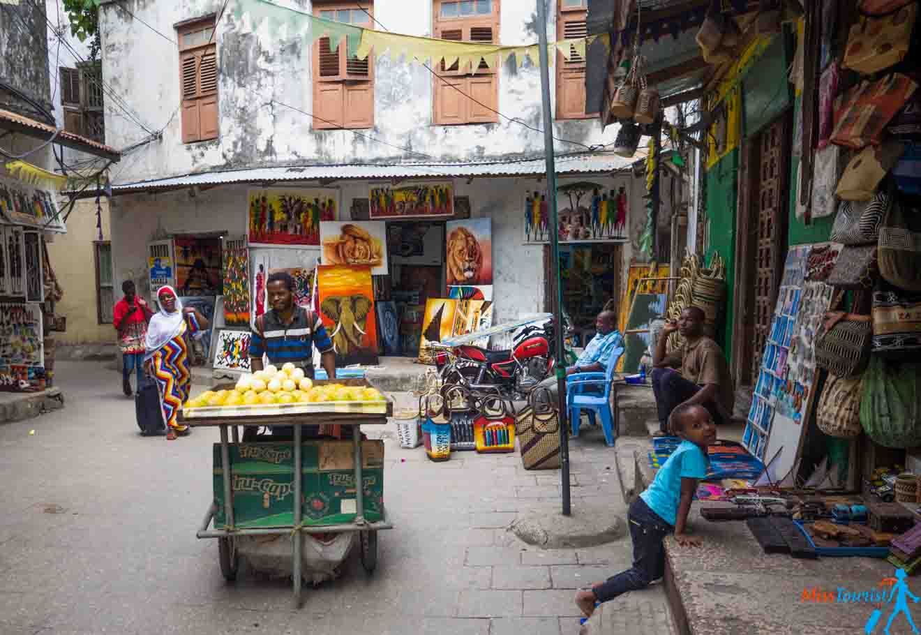 A street in Stone Town with people selling fruit, magnets, paintings and other items.