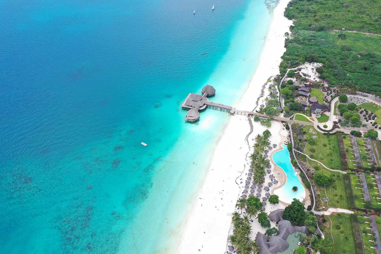 An aerial view of a beach in Zanzibar with a resort with overwater bungalows