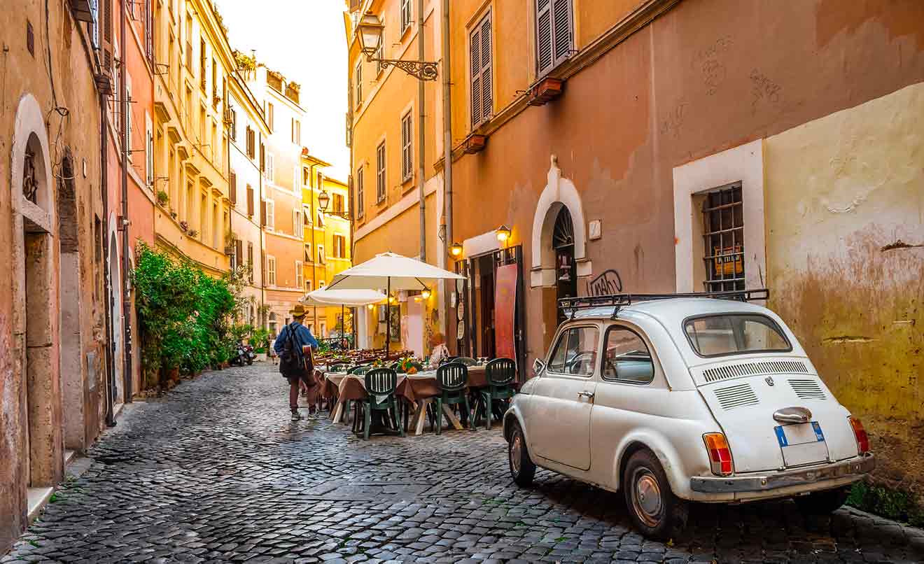 A white car is parked on a cobblestone street in rome.