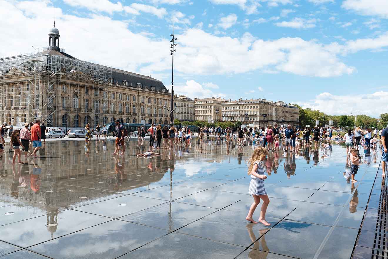 A group of people playing in the Miroir d'Eau in front of a building in Bordeaux