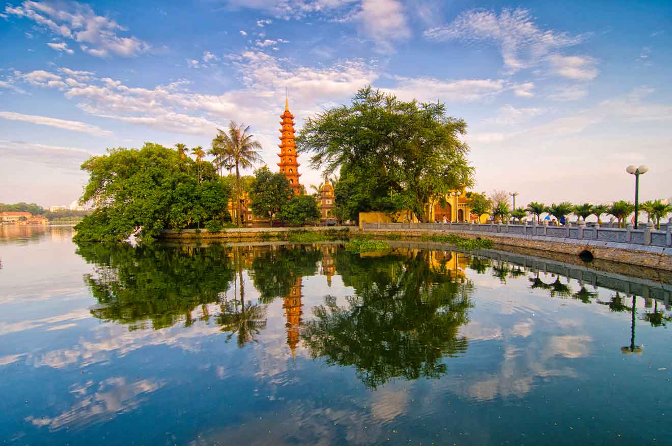 Tran Quoc Pagoda on a peaceful lake in Hanoi at sunrise, reflecting on the water with lush trees surrounding the sacred site, conveying a sense of serenity