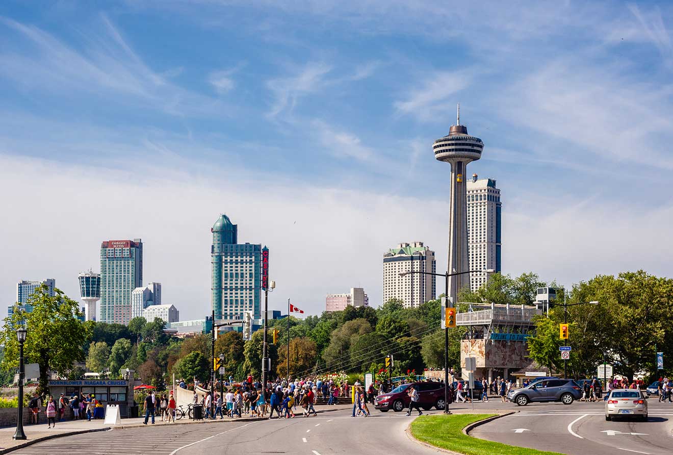 Bustling street intersection with pedestrians and traffic in front of the distinctive skyline of Niagara Falls city, including the Skylon Tower.