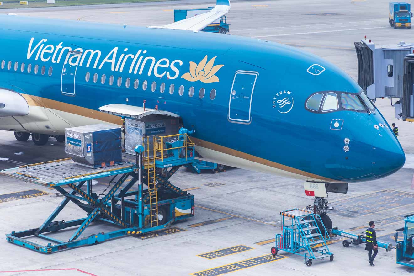 Vietnam Airlines aircraft being serviced on the tarmac, with cargo being loaded, showcasing the airline's vibrant blue livery and modern aviation activity