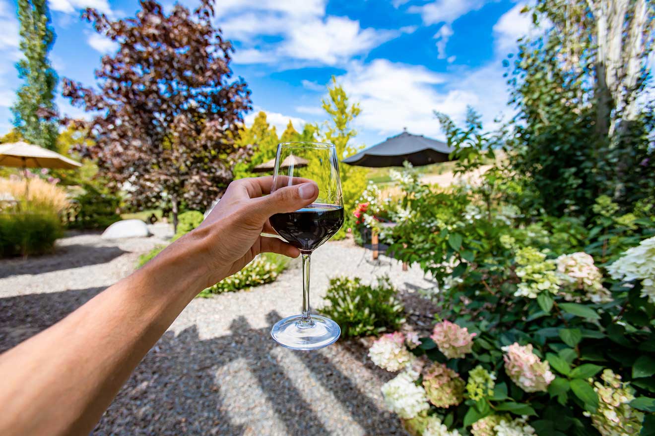 A hand holding a glass of wine in the garden of a Bordeaux winery.