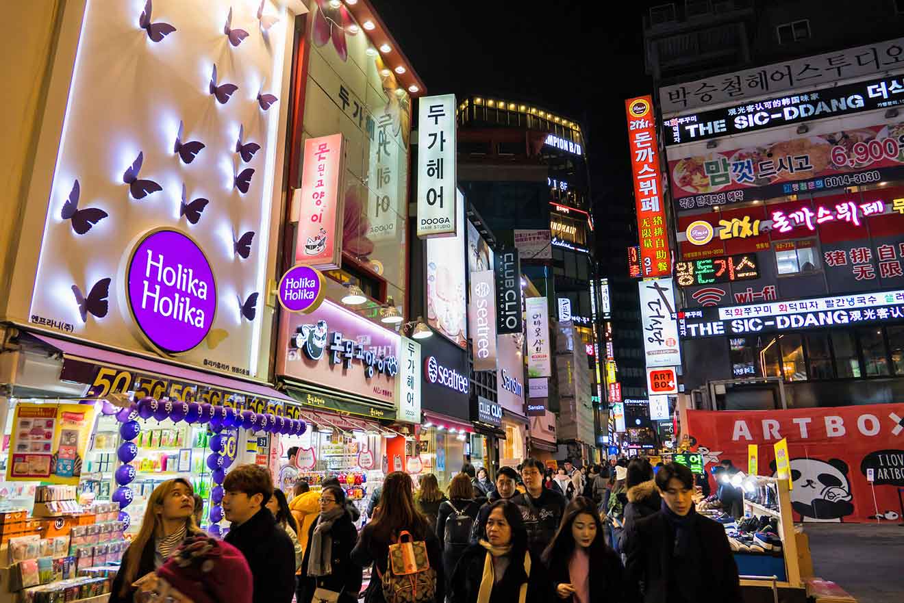 People walking down a street with shops with many neon signs at night in the Myeongdong area in Seoul