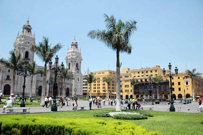 The plaza in front of the cathedral is full of people and palm trees in Lima