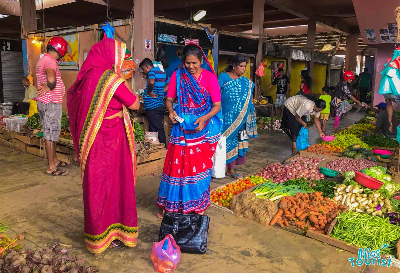 A bustling local market scene with people in colorful traditional clothing shopping for a variety of fresh vegetables laid out on tables, creating a vivid tapestry of daily life and culture.