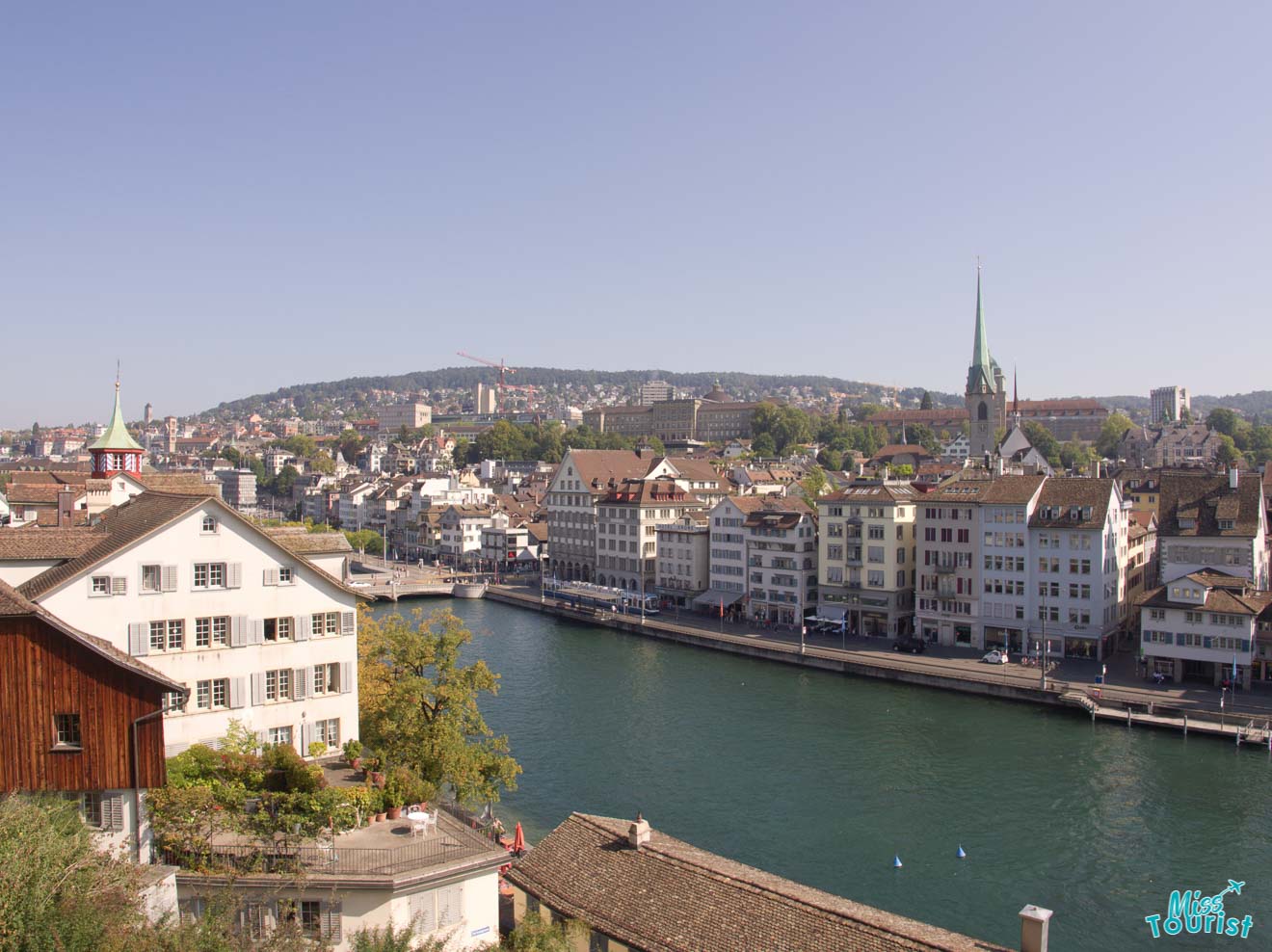 A scenic view of the Limmat river flowing through the historic center of Zurich, with a clear view of the Grossmünster church and surrounding old town buildings