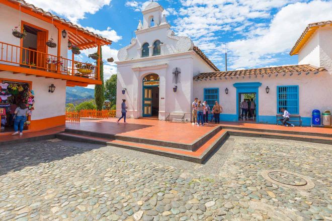 Traditional white church and colorful colonial buildings in a cobblestone square in Medellin