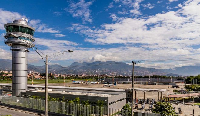 View of an airport control tower at Medellin airport overlooking the tarmac with aircraft and the cityscape against a backdrop of mountains