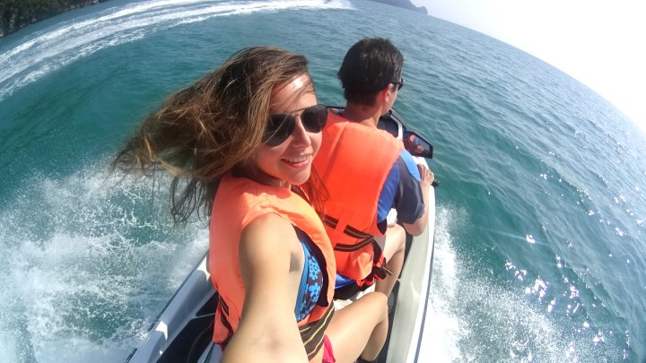 A selfie of  the author of the post on a speedboat, on of whom is the writer of the post smiling at the camera with windblown hair, wearing an orange life vest with the ocean in the background.