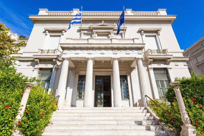 The facade of a neoclassical building in Athens adorned with Greek flags, representing the elegance found within the city's architecture.