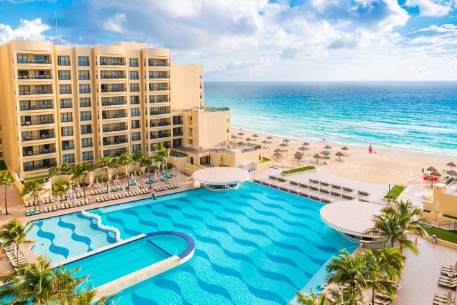 Luxurious beachfront resort in Cancun, with an expansive pool area leading to a pristine beach and the vast blue ocean, under clear skies