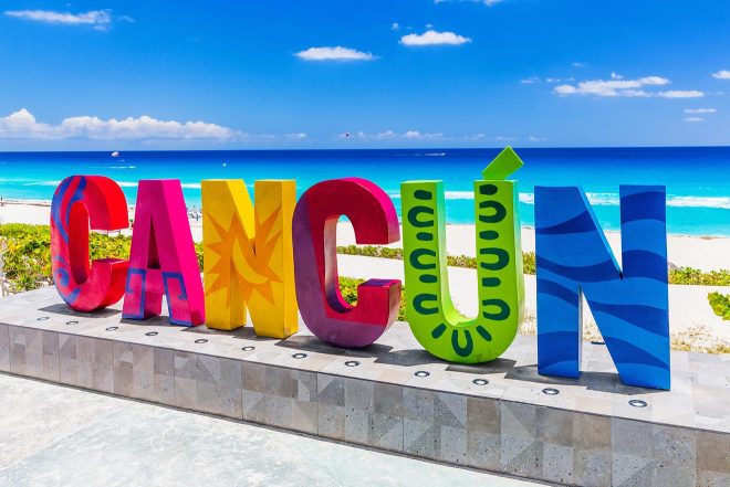 Colorful three-dimensional 'CANCUN' sign on a sunny day with clear blue skies and a turquoise ocean in the background, symbolizing the vibrant tourist destination of Cancun, Mexico