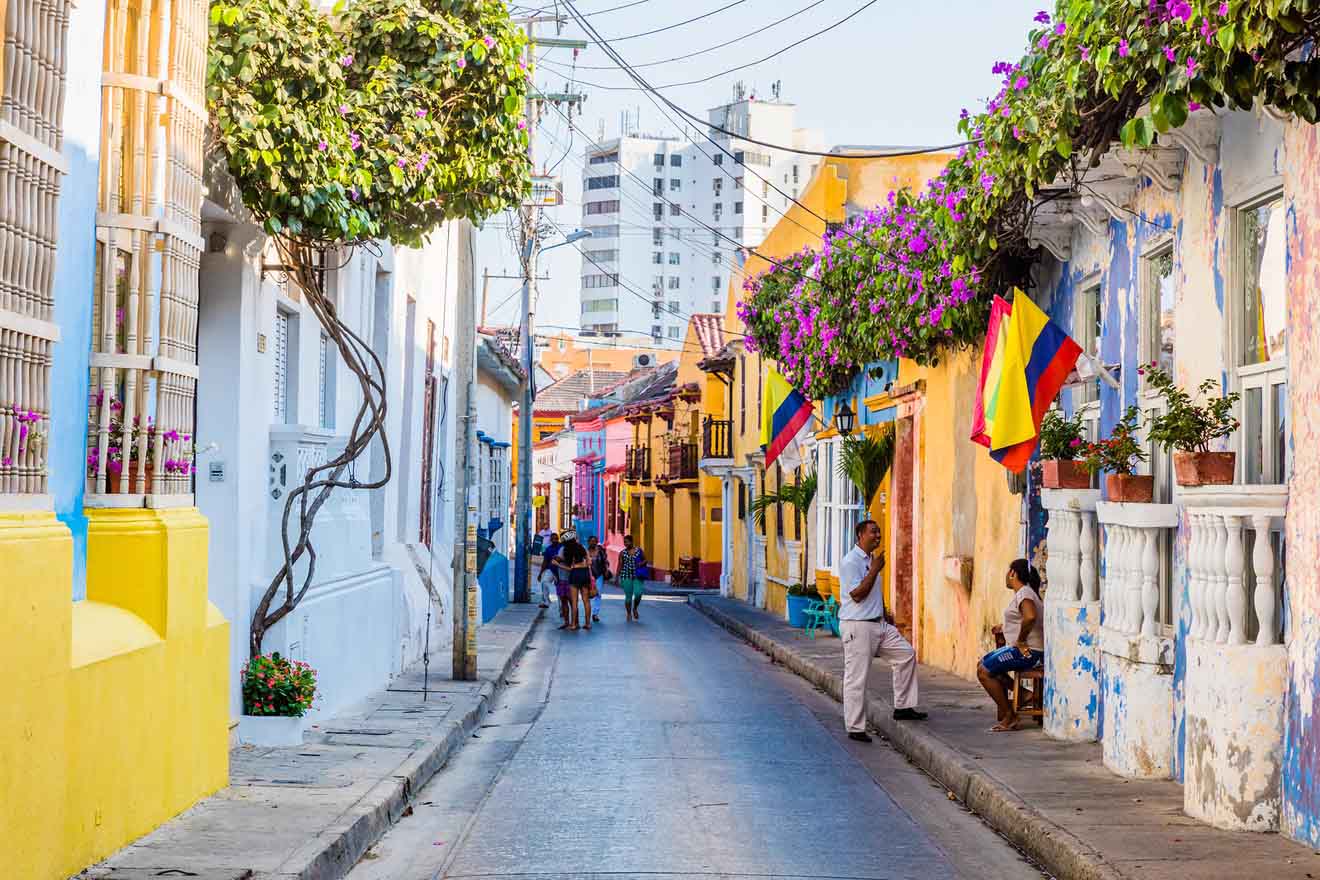 Colorful street view in a vibrant neighborhood in Cartagena with colonial buildings, overhead bougainvillea, and Colombian flags, capturing the essence of a lively Latin American city.