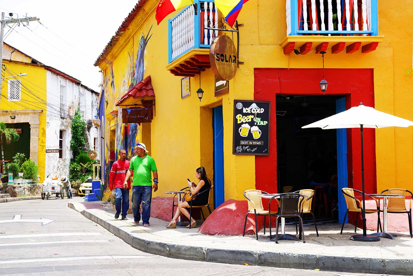 Vivid street scene in Cartagena with colorful murals, local businesses, and residents engaging in daily life under the bright facade of Latin American culture