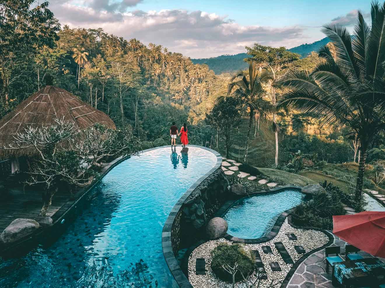 Two people standing on the edge of a pool in the jungle.