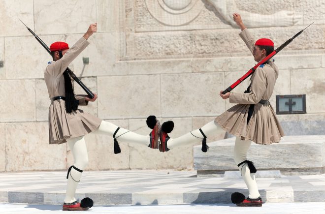Two Greek Evzones soldiers performing the traditional changing of the guard ceremony in front of a historical monument, showcasing cultural heritage in their distinctive uniforms