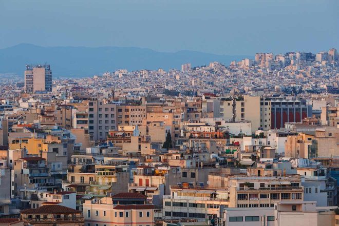 Dusk view of Athens cityscape showing dense residential buildings and the glow of the setting sun softening the urban landscape.