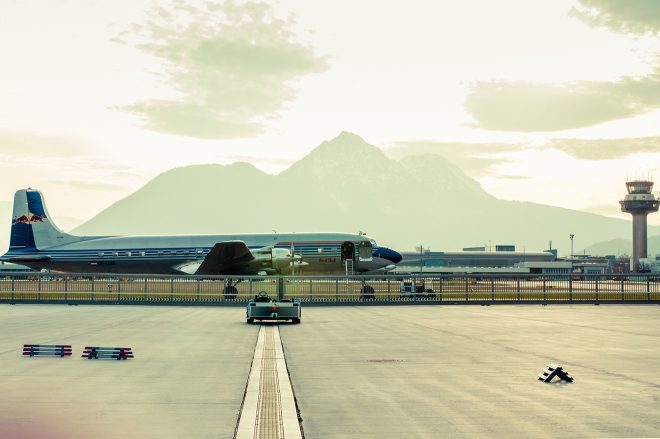 Tarmac of Salzburg Airport with a small plane, tower, and the mountains in the distance