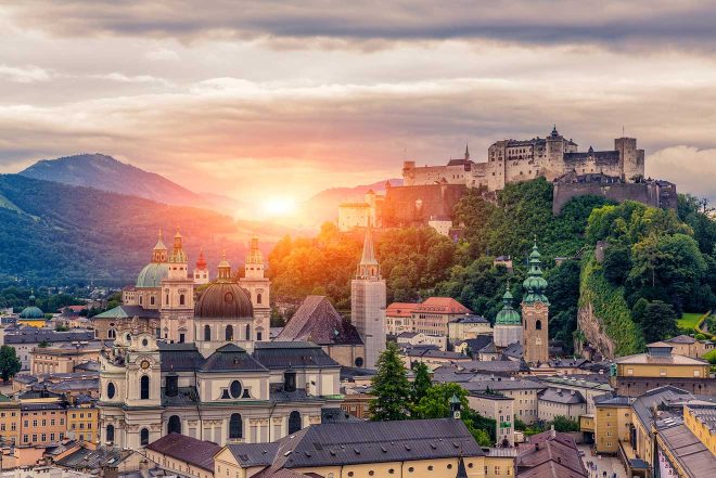 Sunset over Salzburg Castle, with the city's historical architecture in the foreground