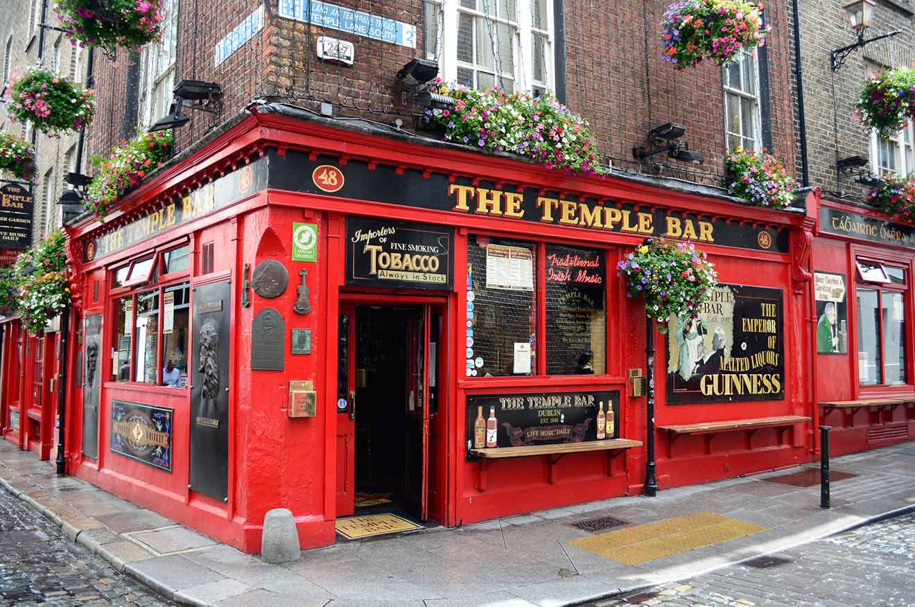 Iconic red facade of The Temple Bar in Dublin, adorned with hanging flower baskets, vintage signage, and gold lettering