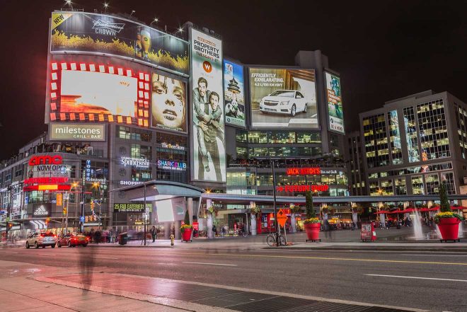 Evening scene at Toronto's Dundas Square, with bright billboards, urban storefronts, and bustling street activity under city lights