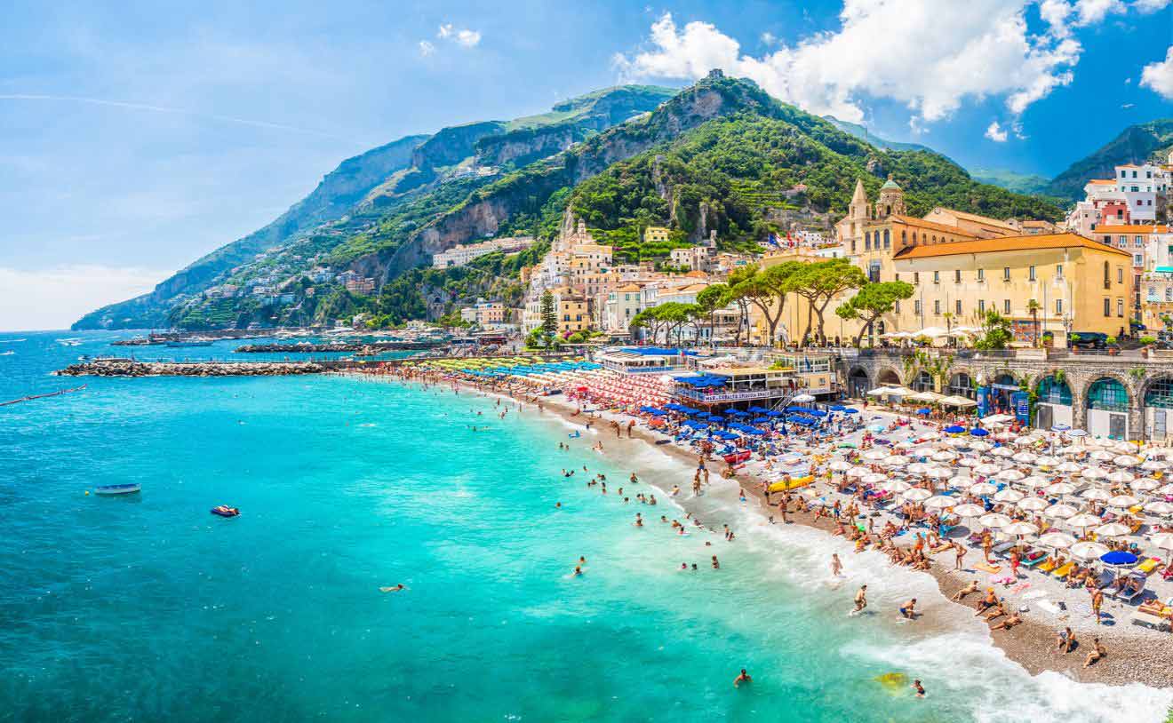 The beach on the Amalfi coast in Italy with many umbrellas, lounge chairs, and people