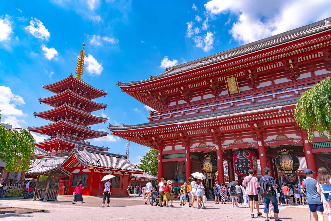 The historic red architecture of Senso-ji Temple in Asakusa, Tokyo, with visitors milling around the entrance