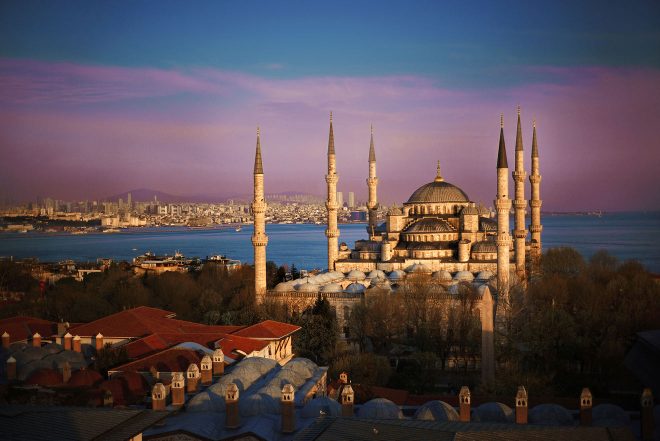 The Blue Mosque in Istanbul captured at dusk with the city's skyline in the background, highlighted by the warm glow of the sunset