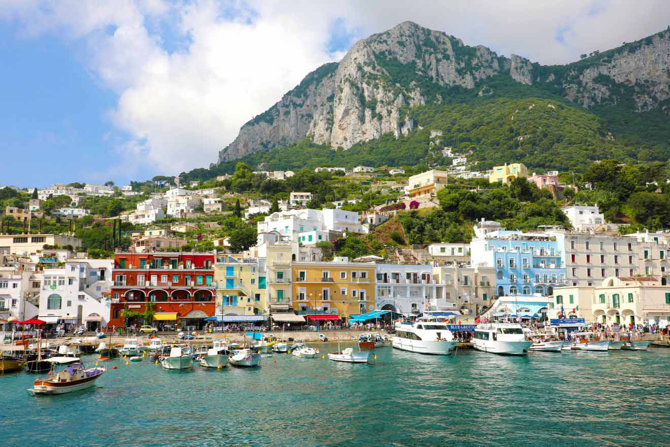 Boast docked on the Marina Grande Harbor on Capri Island on the Amalfi Coast in Italy with colorful houses aligned on the coast and mountains in the background