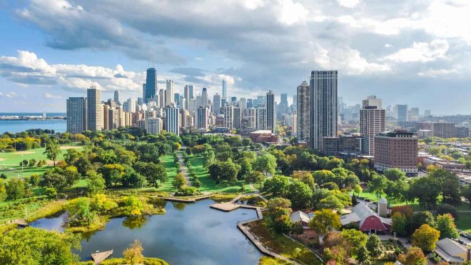 Scenic view of Chicago's skyline overlooking a lush green park with a pond, under a partly cloudy sky.
