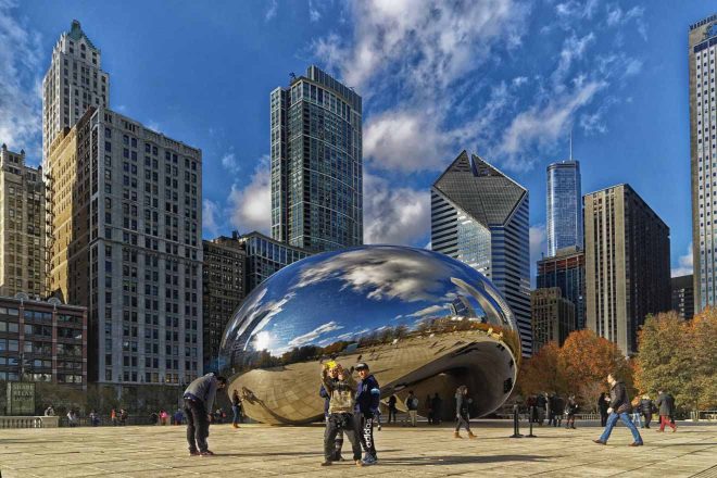 Visitors around the reflective 'Cloud Gate' sculpture in Chicago's Millennium Park on a sunny day with clear blue skies and surrounding skyscrapers